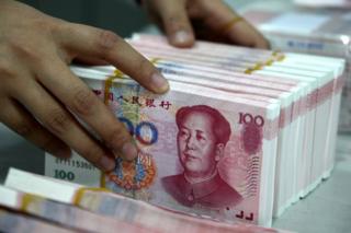 Chinese bank teller counts stacks of Chinese 100-yuan (one hundred yuan) notes at a bank in Huaibei, east China's Anhui province on 12 November 2010