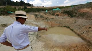 Hombre con sombrero señala un lugar donde se realizó una excavación.