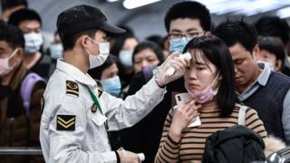 Un agente de seguridad tomando la temperatura a una mujer en China.