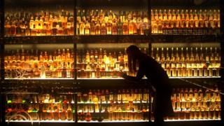 A woman examines bottles of Scotch whisky on a set of shelves