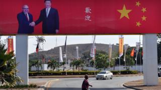 A woman crosses a road with a billboard, showing Papuan-New Guinean Prime Minister Peter O Neill (top left) shaking hands with Chinese President Xi Jinping and the message 