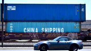 A motorist drives past shipping containers, including one from China Shipping, a shipping conglomerate under direct administration of China's State Council, awaiting transportation on a rail line at the Port of Long Beach on July 12, 2018 in Long Beach, California
