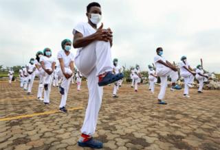 Dozens of masked male and female health workers stand in formation as they stretch in sync.