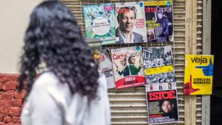 Mulher passando diante de banca de revista no Brasil