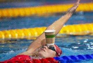 Jenny Mensing of Germany swims backstroke with a paper cup on her forehead while warming up at the Glasgow 2018 European Swimming Championships in Glasgow, UK