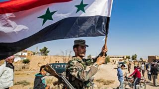 A Syrian regime soldier waves the national flag