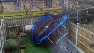 A trampoline which has been blown into a garden