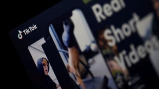 TikTok's website is seen in this photo, showing someone doing a handstand and another person wearing sunglasses in sample videos