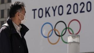 A pedestrian wearing a mask walks past the emblem of Tokyo 2020 Olympics in Tokyo.