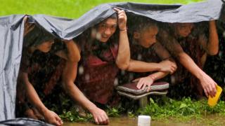 Buddhist monks take shelter under a tarpaulin sheet
