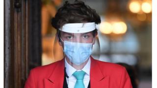 An employee wearing personal protective equipment (PPE) including a face mask and a visor staffs the entrance to up-scale department store Fortnum and Mason on Piccadilly in central London.