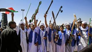 Supporters of Sudan"s President Omar al-Bashir raise up sticks and swords in salute as they gather during a rally for him in the Green Square in the capital Khartoum on January 9, 2019