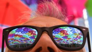 The reflection of colourful umbrellas in a person's sunglasses