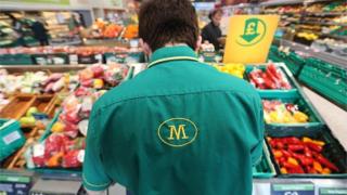 Сотрудник работает на витрине со свежими овощами в супермаркете Morrisons,