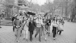 Girls with large brooms walking through New York