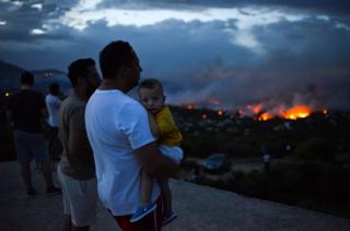 A man holds his son as a wildfire burns in the town of Rafina, near Athens.