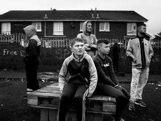 A group of youths and adults congregate in a residential street