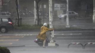 A motorist holds on to a post as she braves high winds and rain of Super Typhoon Meranti in Kaohsiung, southern Taiwan, 14 September 2016.