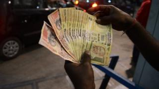 Индийский служащий заправочной станции проверяет банкноты на 500 и 1000 рупий, поскольку жители стоят в очереди на заправочной станции в Силигури 8 ноября 2016 года.