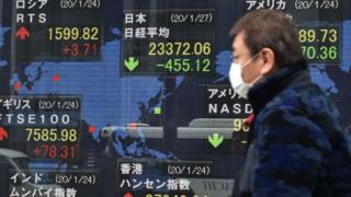 Man in mask walks past share display board