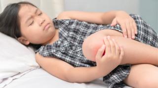 Niña acostada sobándose la rodilla