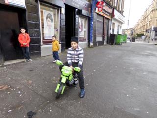 Three boys in the street and one on a green bike