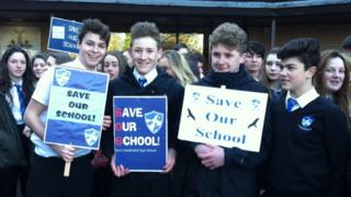 ученики держат плакаты «Спасите нашу школу» на митинге у здания совета