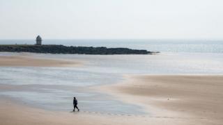 A woman walks alone on Trecco Bay Beach, in Porthcawl, Wales