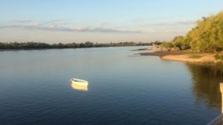 Un bote blanco en una calmada laguna en la que se refleja el cielo, los árboles y el mismo bote