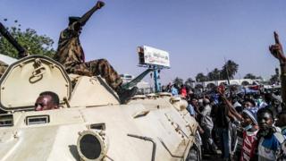Суданские протестующие приветствуют военную бронетехнику, когда они собираются во время демонстрации перед военным штабом в столице страны Хартуме, 9 апреля 2019 года