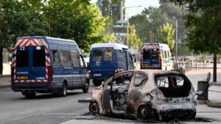 Police vehicles near a burnt car in Dijon