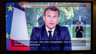 Emmanuel Macron delivering his address to the nation on a television screen
