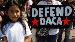 Una niña posa al lado de un cartel que dice: "Defendamos DACA", en inglés
