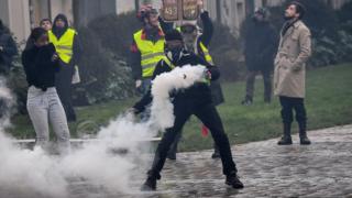 Протестующий - одетый в закрытое лицо, которое должно быть запрещено, - 19 января отбрасывает газовый баллон с полицией