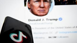 TikTok logo on phone in front of Donald Trump's Twitter feed on a PC screen.