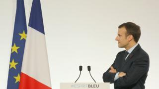Emmanuel Macron staring at French and EU flags