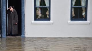 A resident of York stands on her doorstep beside a flooded street