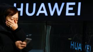 Изображение файла: Женщина использует свой телефон, когда она проходит мимо магазина Huawei в Пекине, Китай.