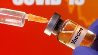 A small bottle labeled with a "Vaccine" sticker is held near a medical syringe