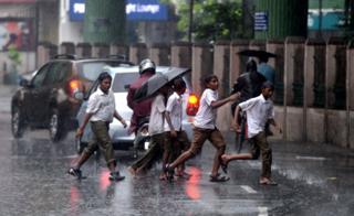Indian school students cross the street under monsoon rains in Chennai