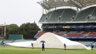 Ground staff pull a cover over the pitch at the Adelaide Oval because of rain