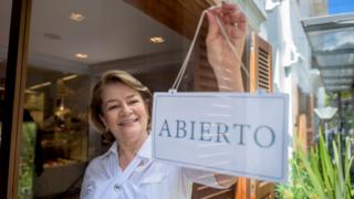 Una mujer sostiene un cartel en un comercio que dice "abierto".