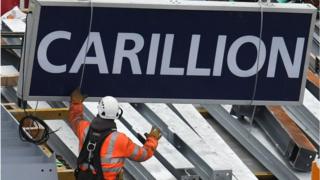 A construction worker guides a Carillion sign being lowered to the ground