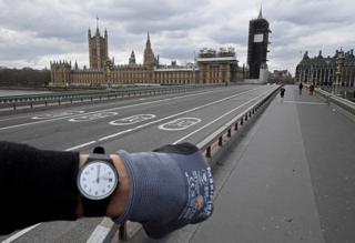 A photographer wearing a watch at noon in front of the Houses of Parliament on Westminster Bridge, in London, UK