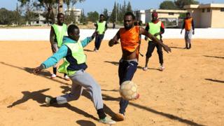 Cameroonian (orange) and Senegalese (yellow) African migrants, split into two teams, take part in a football match at the Libyan Interior Ministry's illegal immigration shelter in Tajoura,