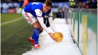 Ipswich Town football player James Bree retrieves the ball from a pile of snow at Portman Road.