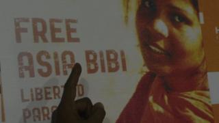 На этой фотографии, сделанной 27 сентября 2016 года, Ашик Масих, муж Азии Биби, христианской женщины, которой грозит смертный приговор за богохульство, указывает на плакат с изображением его жены Азии в жилом районе Лахора.
