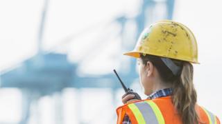 A woman wearing a hard hat and hi-visibility vest at work