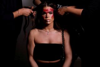 A model is seen sitting whilst her hair is styled