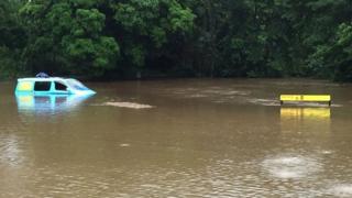 Campervan наполовину погруженный в реку возле знака предупреждения о крокодилах